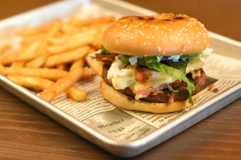 A juicy burger with melted cheese, bacon, and lettuce, served with golden fries on a metal tray.