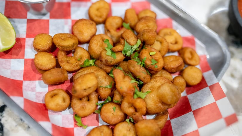 Golden brown fried seafood pieces, some round and some ring-shaped, garnished with cilantro on a red and white checkered paper.