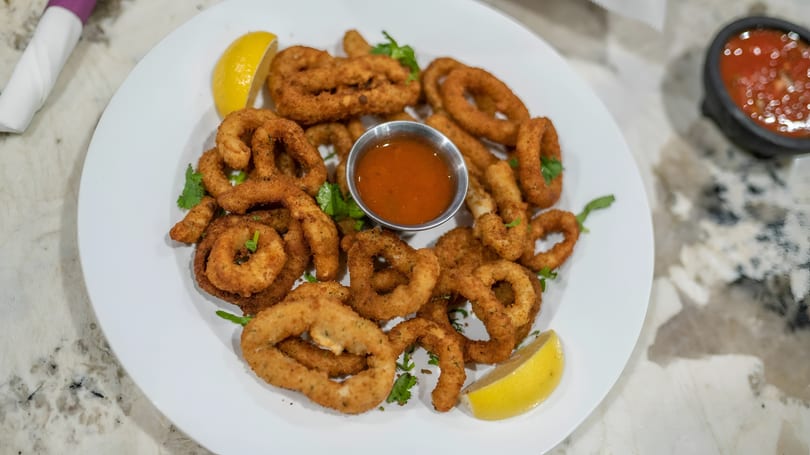 Crispy fried calamari rings and tentacles with a side of red dipping sauce and lemon wedges.