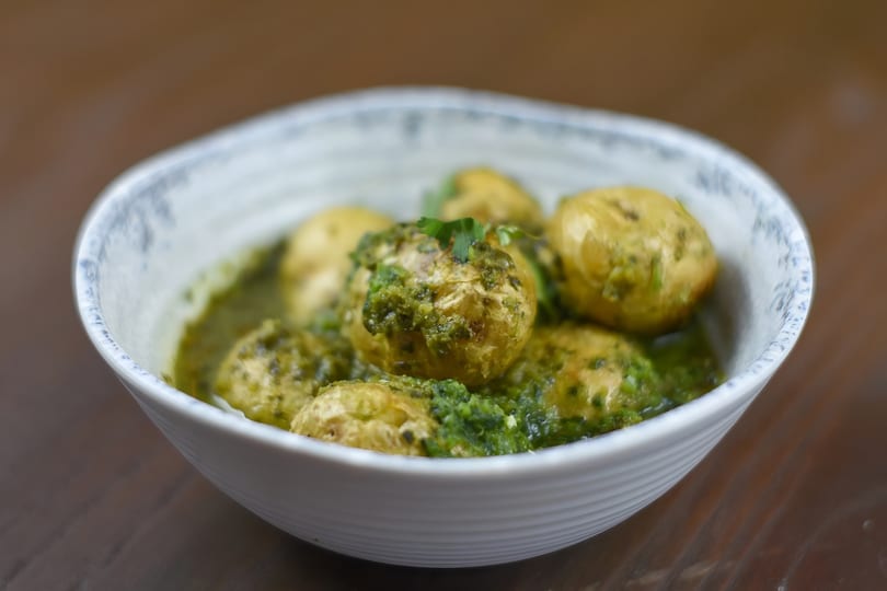 Small, golden potatoes covered in a vibrant green pesto sauce, served in a white bowl.