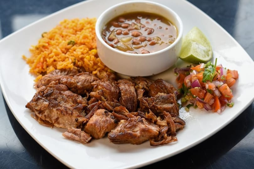 A plate of carnitas with rice, beans, pico de gallo, and a lime wedge.
