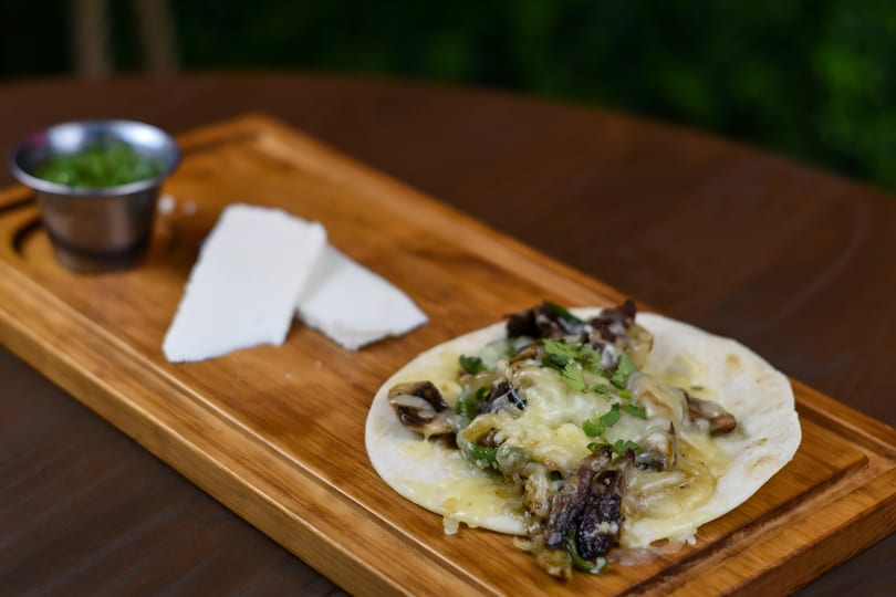 Mushroom and cheese taco with cilantro, served on a wooden board with white cheese and green sauce.