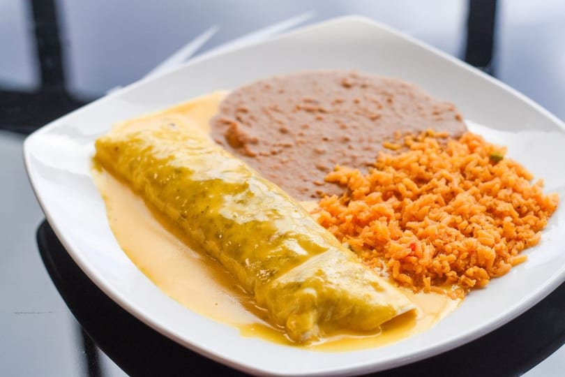 A plate of Mexican food with a green chile enchilada, refried beans, and orange rice.