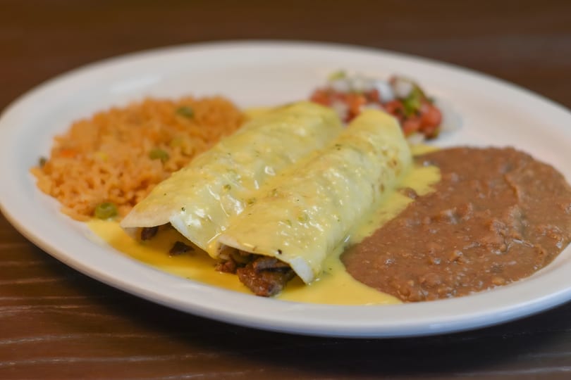 Two enchiladas covered in cheese sauce, served with rice, refried beans, and pico de gallo.