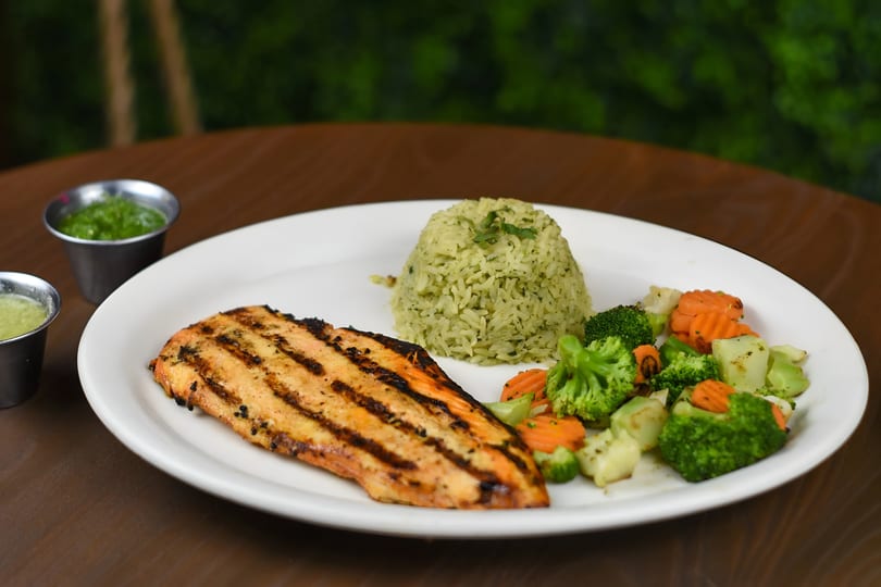 Grilled chicken breast with green rice, steamed broccoli, carrots, and two small sauce cups.