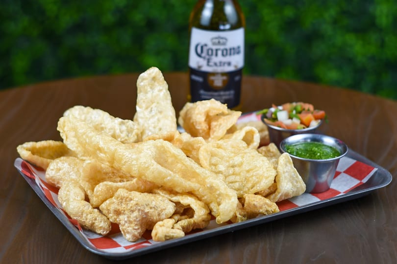 Crispy chicharrones on a tray with salsa and pico de gallo, and a Corona beer.