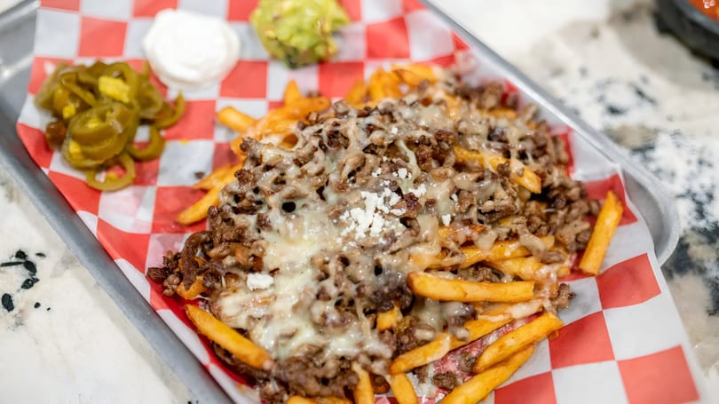 Loaded fries with melted cheese, ground meat, and a side of jalapeños, sour cream, and guacamole.