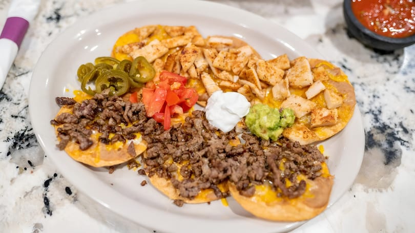 A plate of nachos with ground beef, chicken, jalapeños, tomatoes, sour cream, and guacamole.